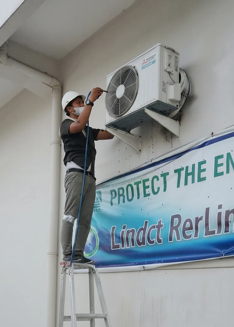 Teknisi memasang unit AC outdoor menggunakan tangga